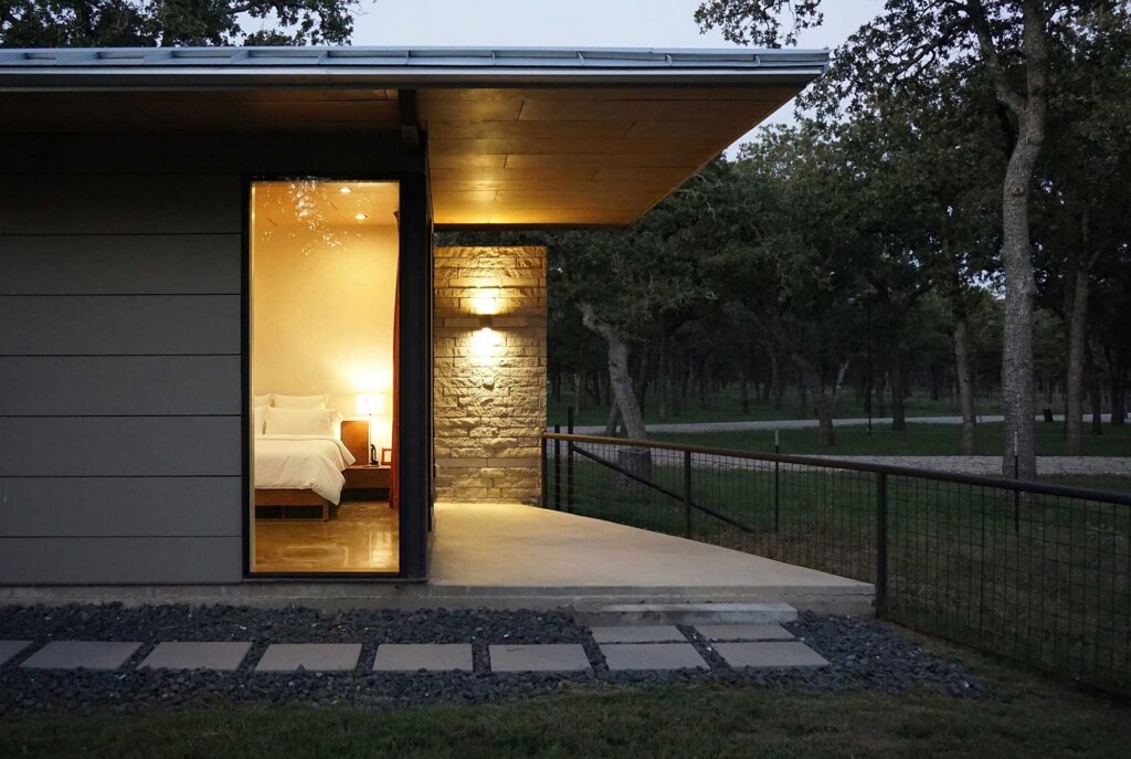 Modern ranch house exterior at dusk with limestone wall, extended roof overhang, and bedroom view