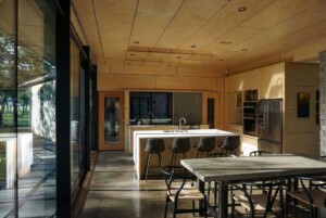 Modern kitchen with plywood ceiling and walls, white island, concrete floors, and floor-to-ceiling