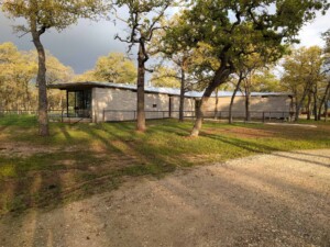 Modern single-story ranch house with stone and metal siding set among oak trees with metal roof