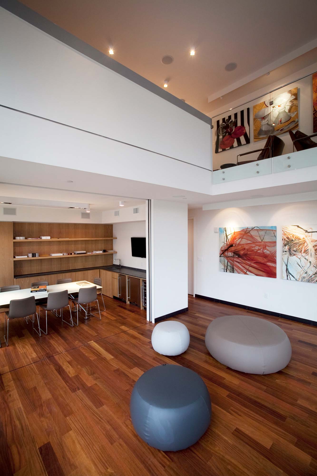 Modern double-height loft interior with wood floors, mezzanine level, abstract art, and minimalist