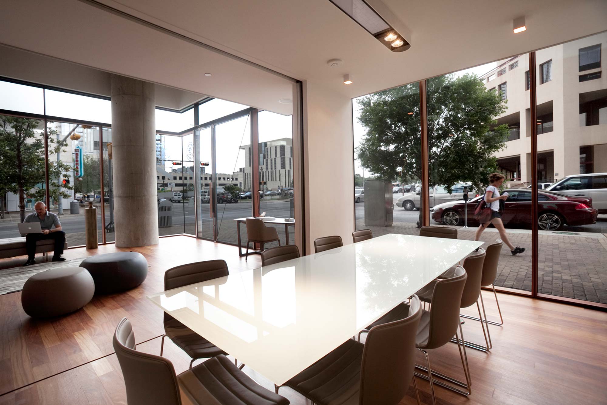 Modern lobby with glass walls, white conference table, leather chairs, concrete column, wood floors