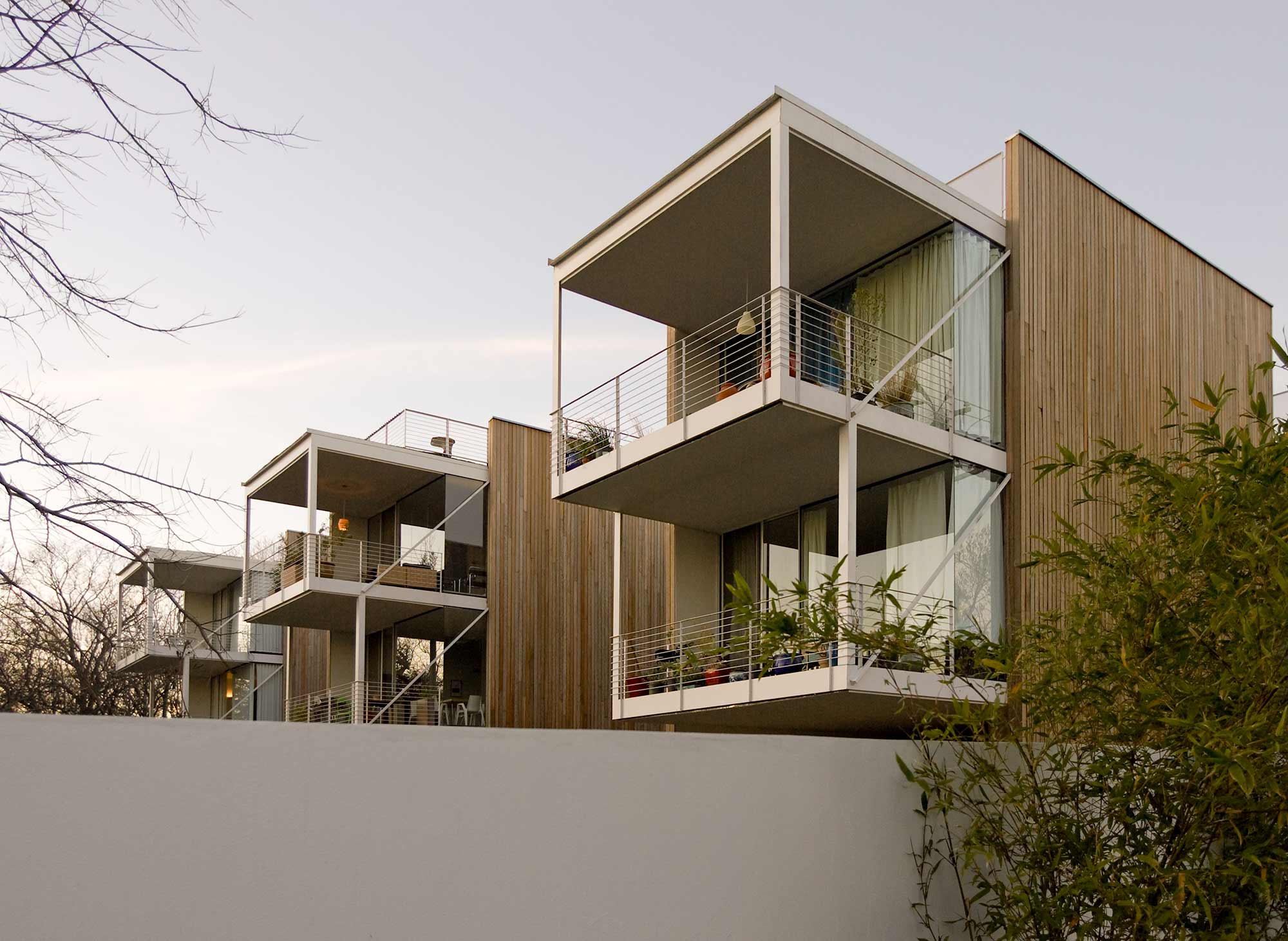 Modern multi-unit residential building with wood cladding, white steel balconies, and large glass