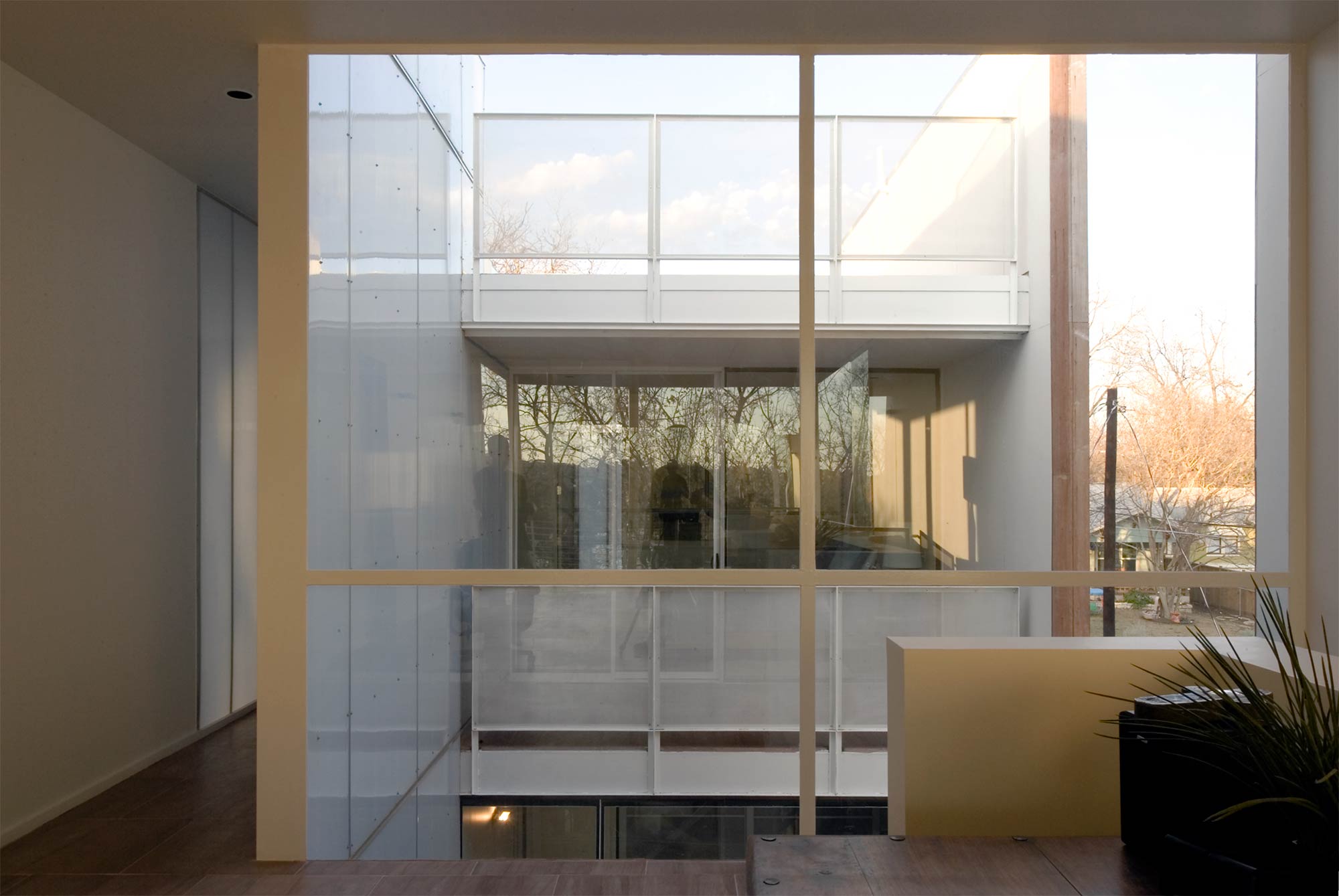 Interior view through large glass windows overlooking a modern courtyard with white balcony and