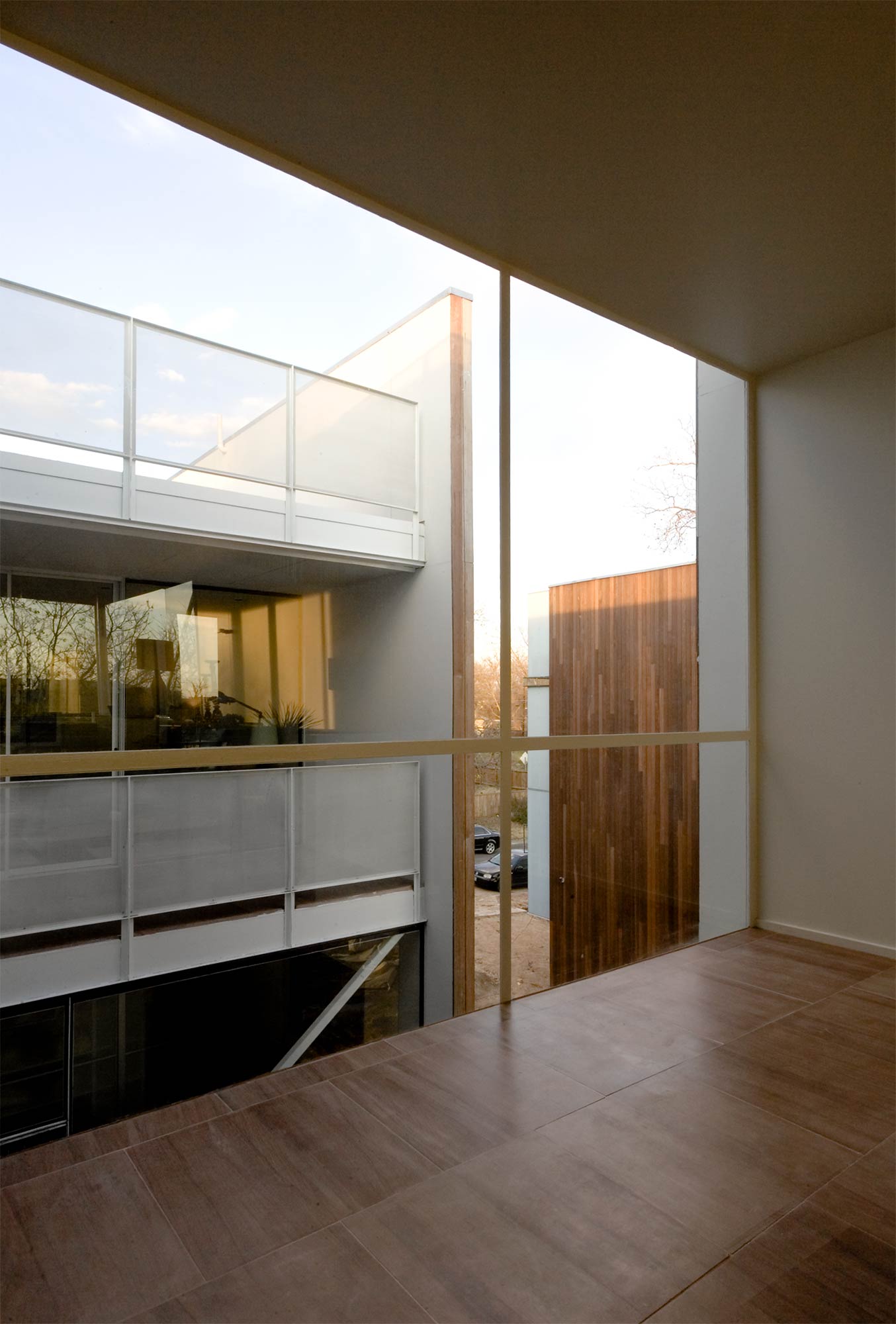 Modern interior view with wood flooring looking out to courtyard with white balcony and wood-clad