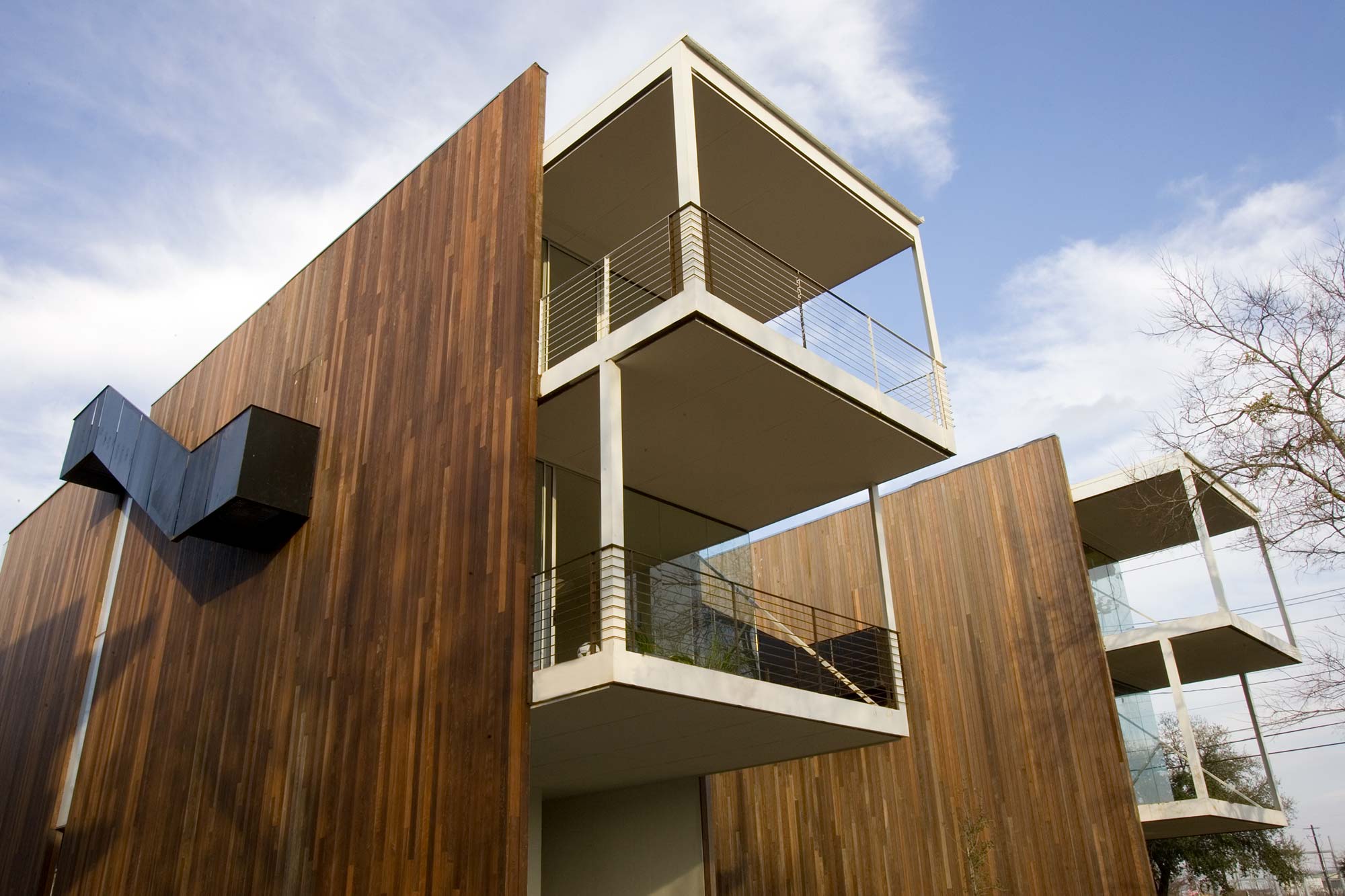 Modern multi-story building with vertical wood cladding and stacked white concrete balconies