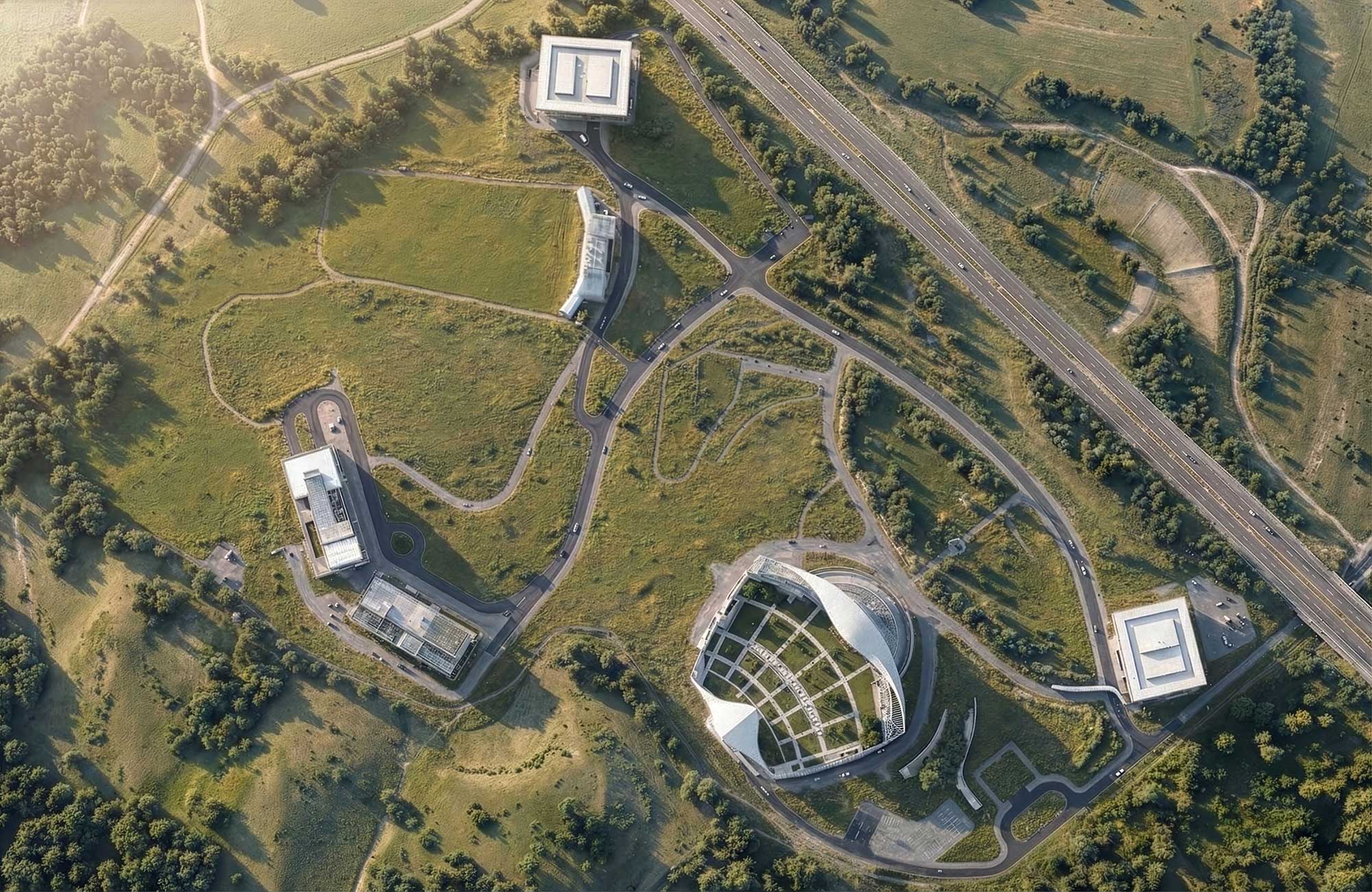 Aerial view of campus with curved organic buildings scattered across green landscape near highway